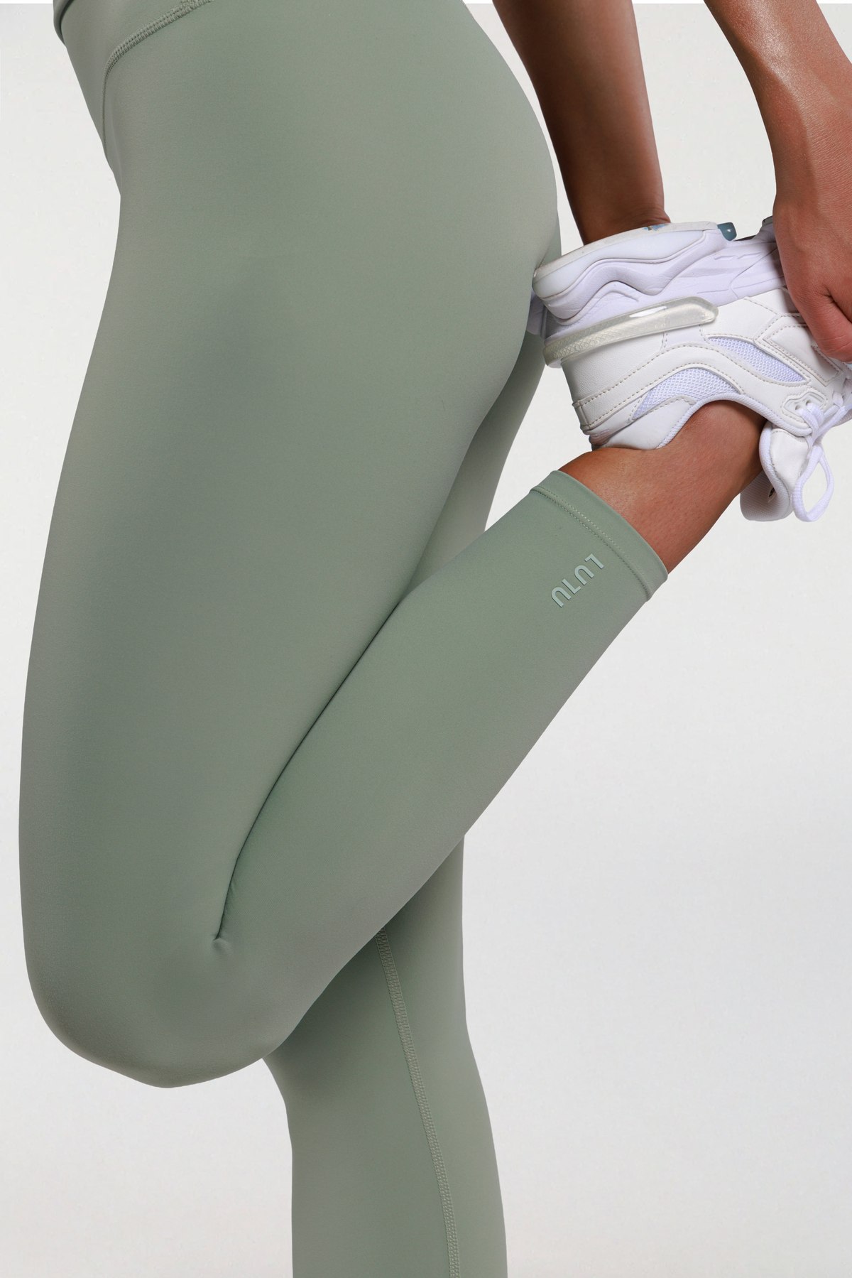 Close-up of the LULU logo on sage green leggings during a stretch