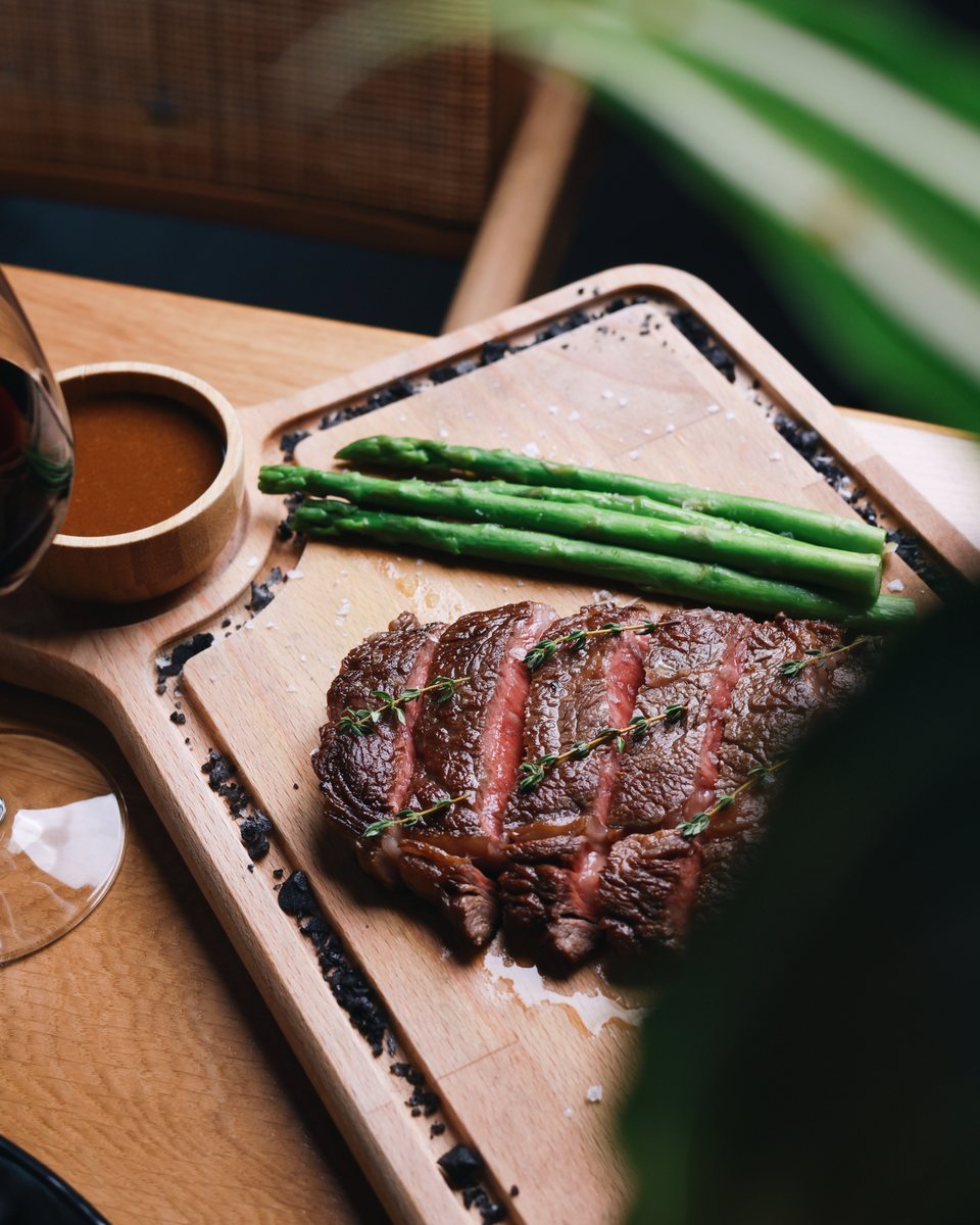 Sliced steak with asparagus and jus on a wooden board