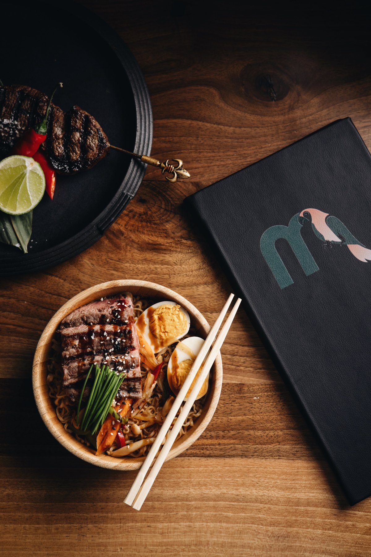 Beef ramen bowl beside the Mayfair menu and grilled skewers