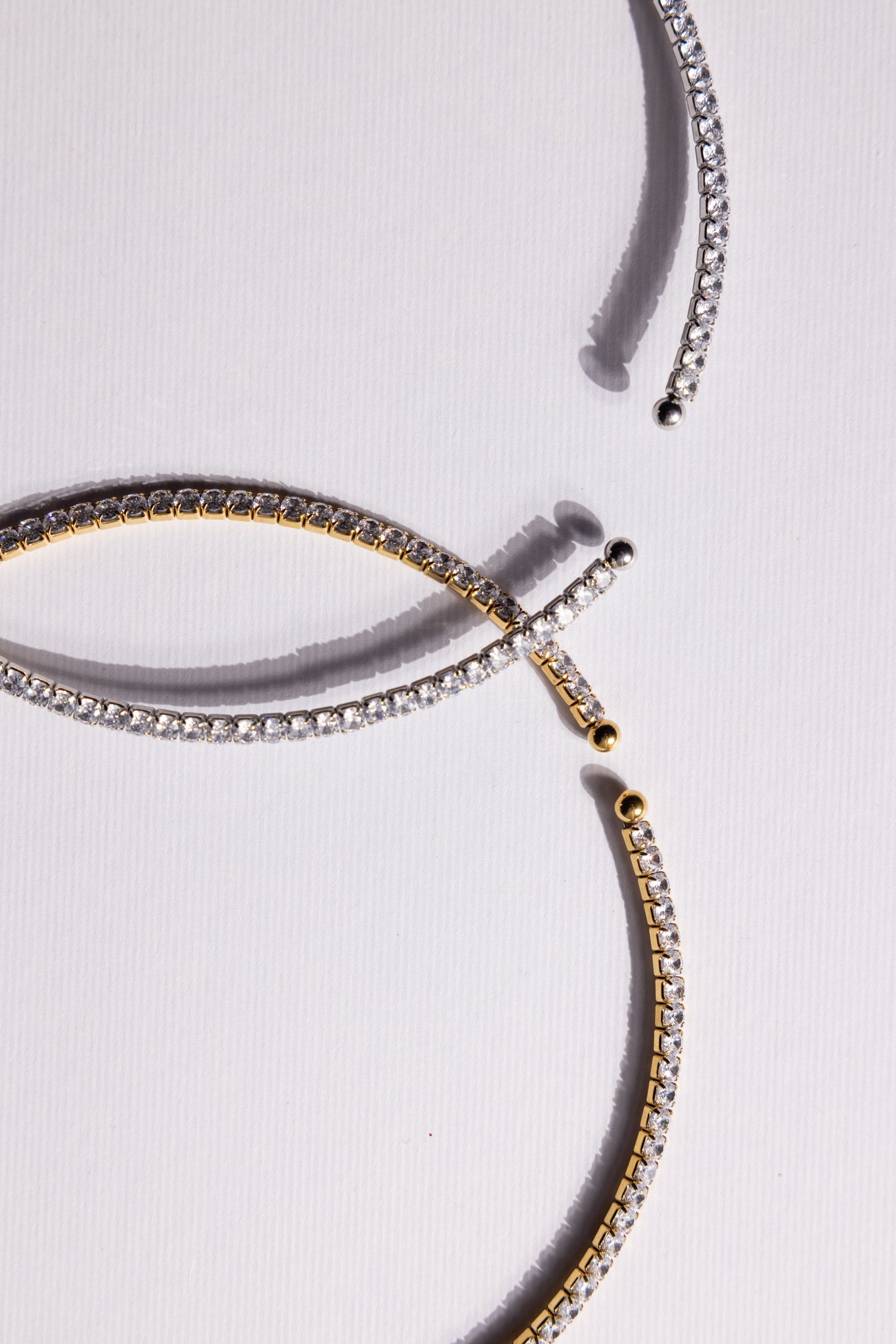 Silver and gold crystal cuff bracelets crossing on textured paper