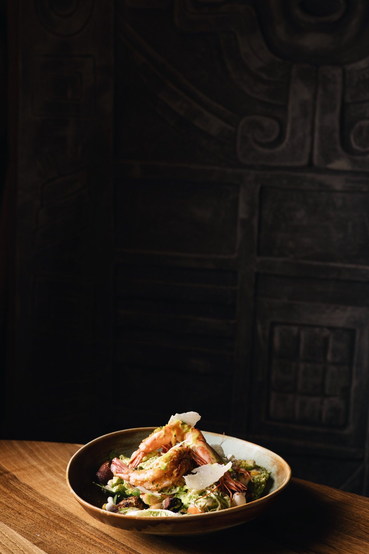 Shrimp salad with shaved parmesan against a carved stone wall