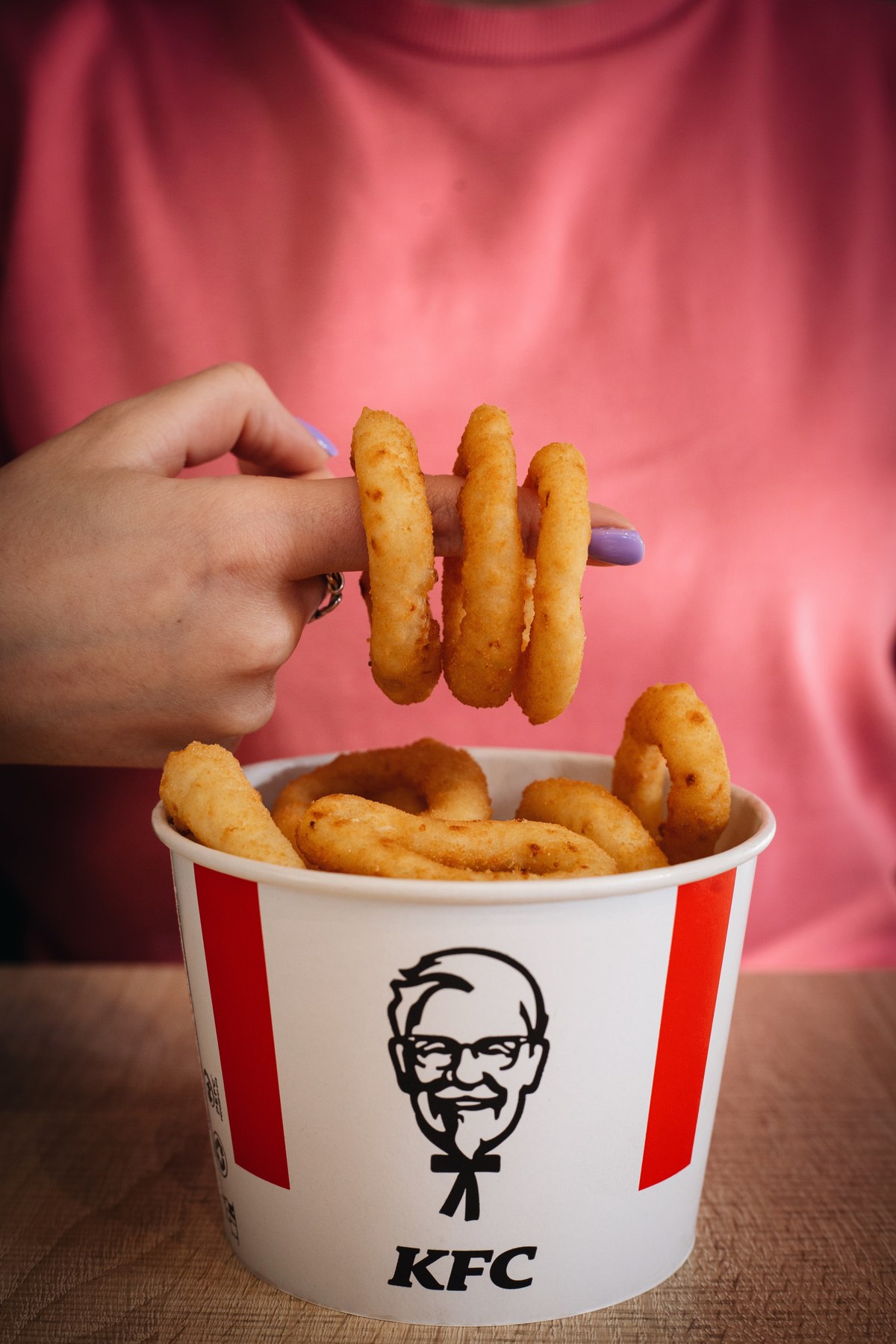 Onion rings stacked on a finger above a KFC bucket