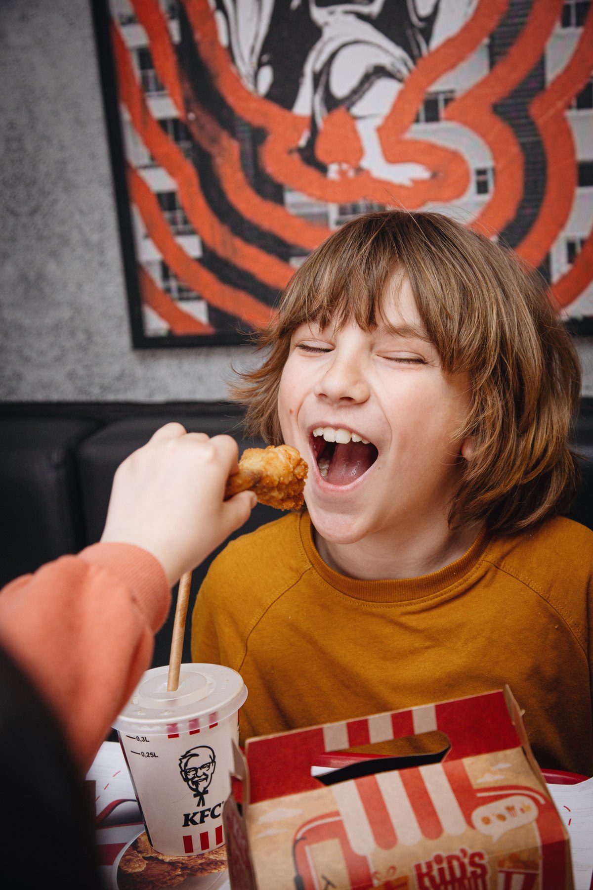 Boy laughing as he is offered a piece of KFC chicken