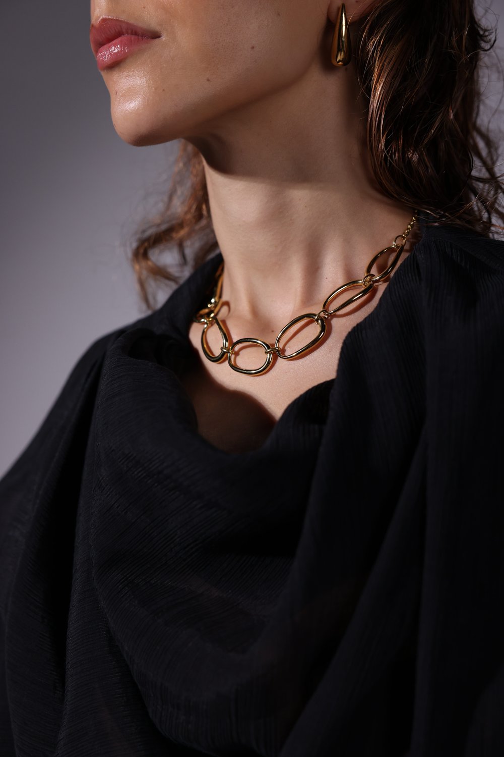 Gold oval link necklace and gold teardrop earring worn with a black draped top