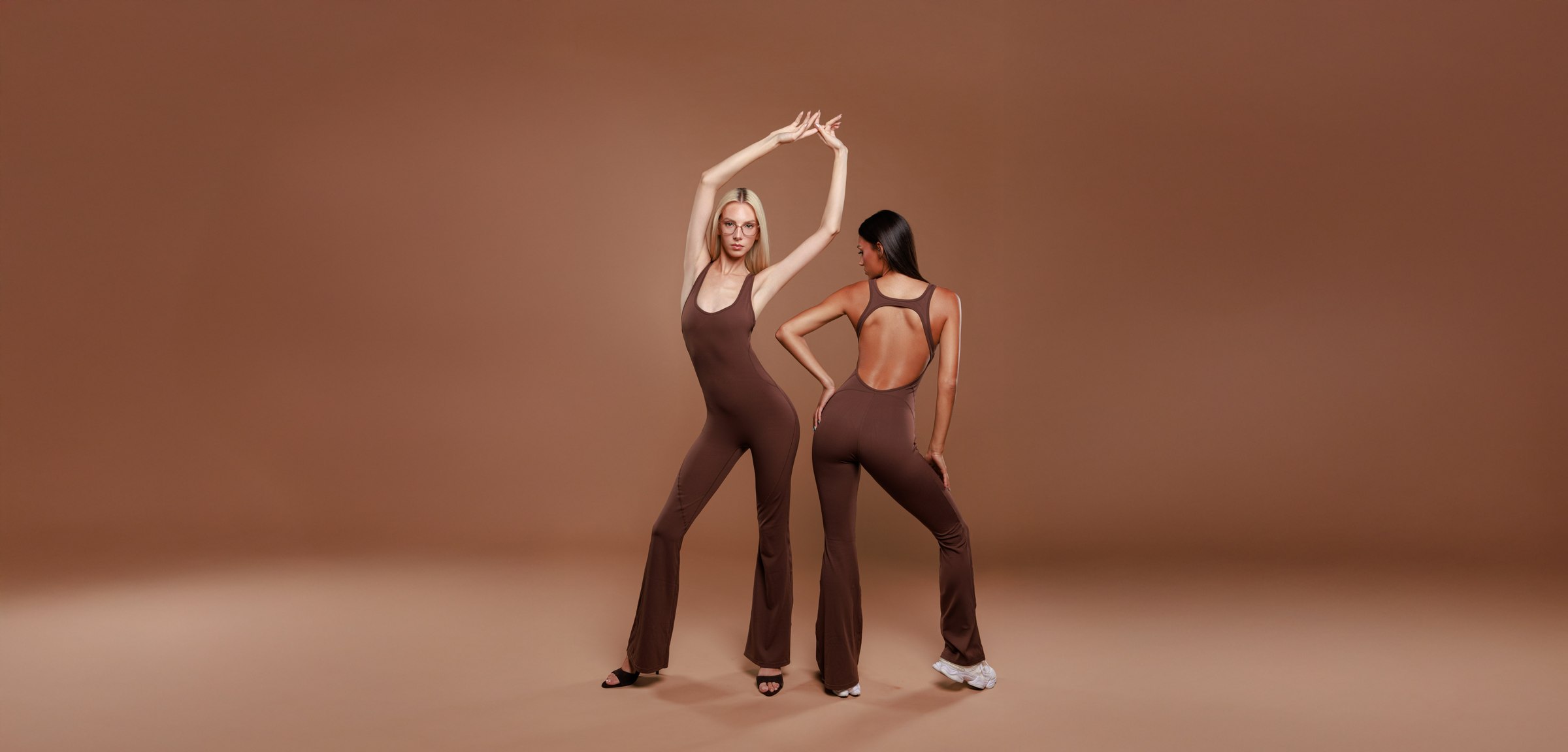 Two models posing in brown LULU flared jumpsuits on a brown backdrop