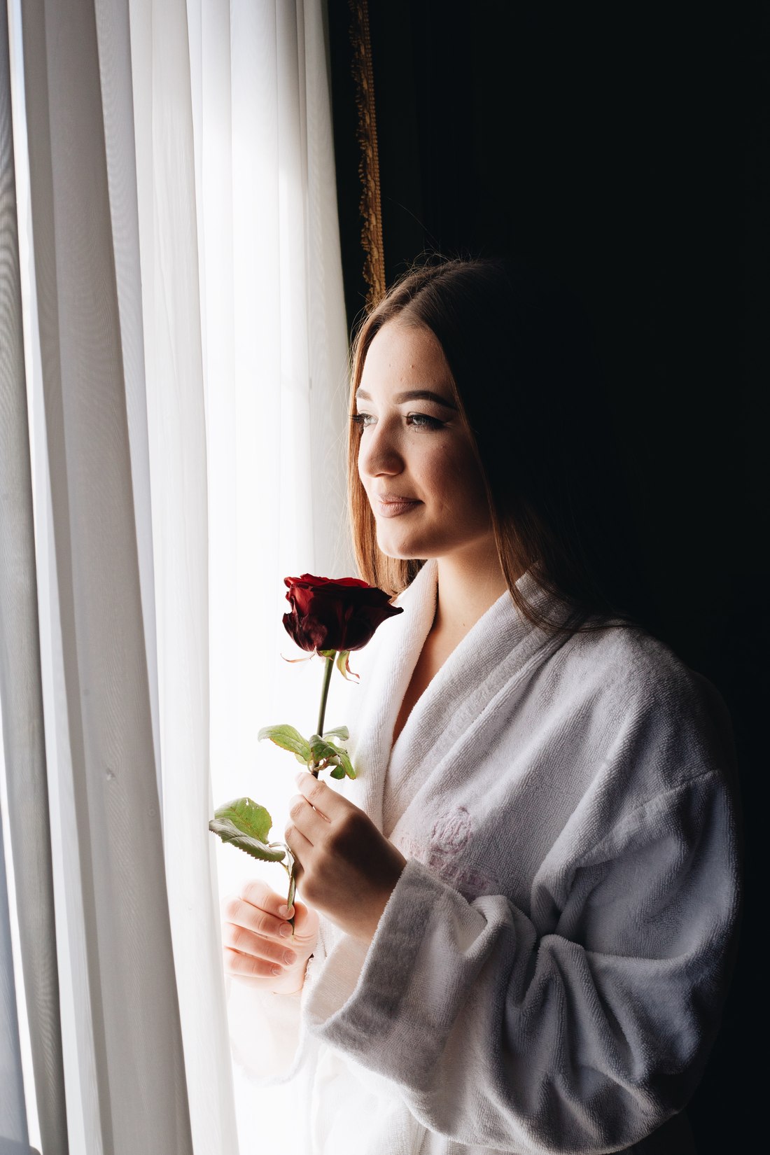 Guest in a hotel robe holding a red rose by the window