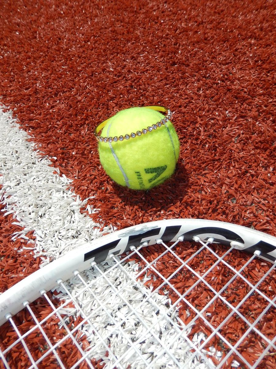 Gold tennis bracelet around a tennis ball on a clay court