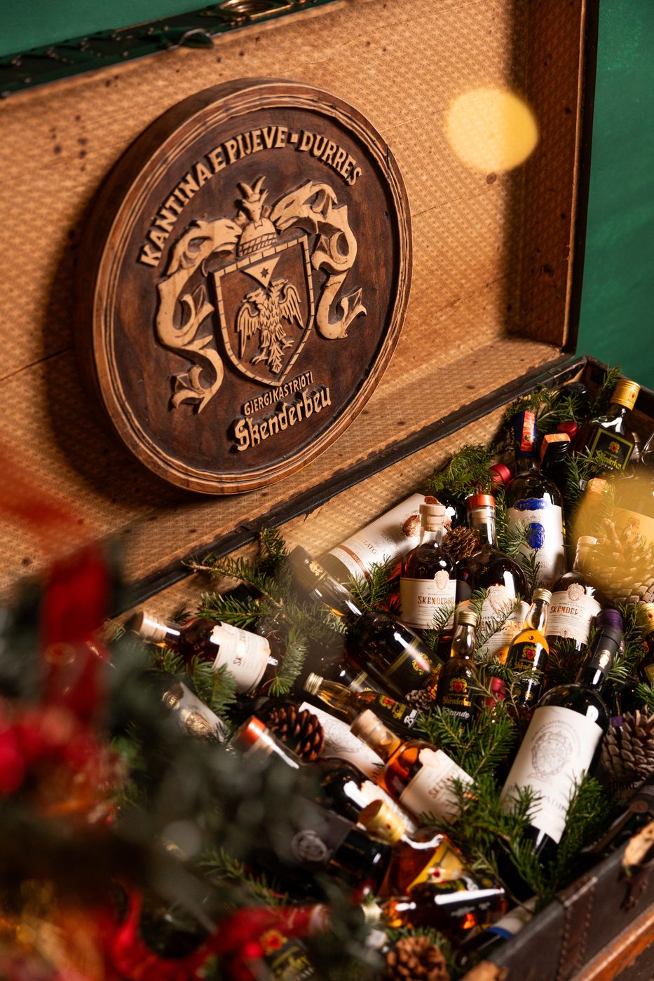 Carved Kantina Skënderbeu crest above a chest of bottles and pine branches