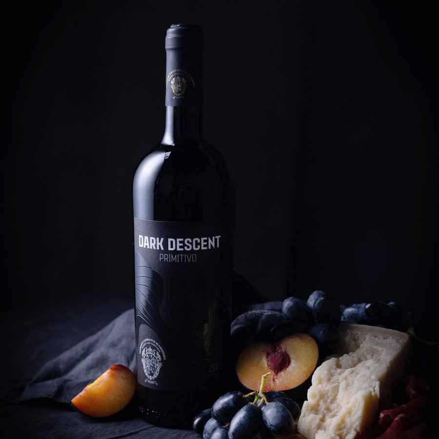 Dark Descent Primitivo bottle with fruit and cheese in low light