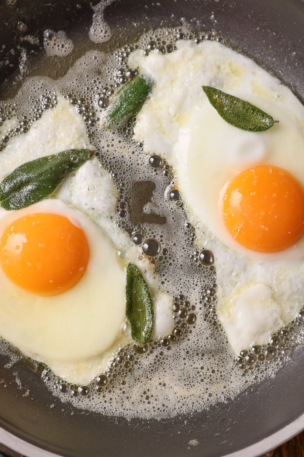 Two AIBA eggs frying in butter with sage leaves