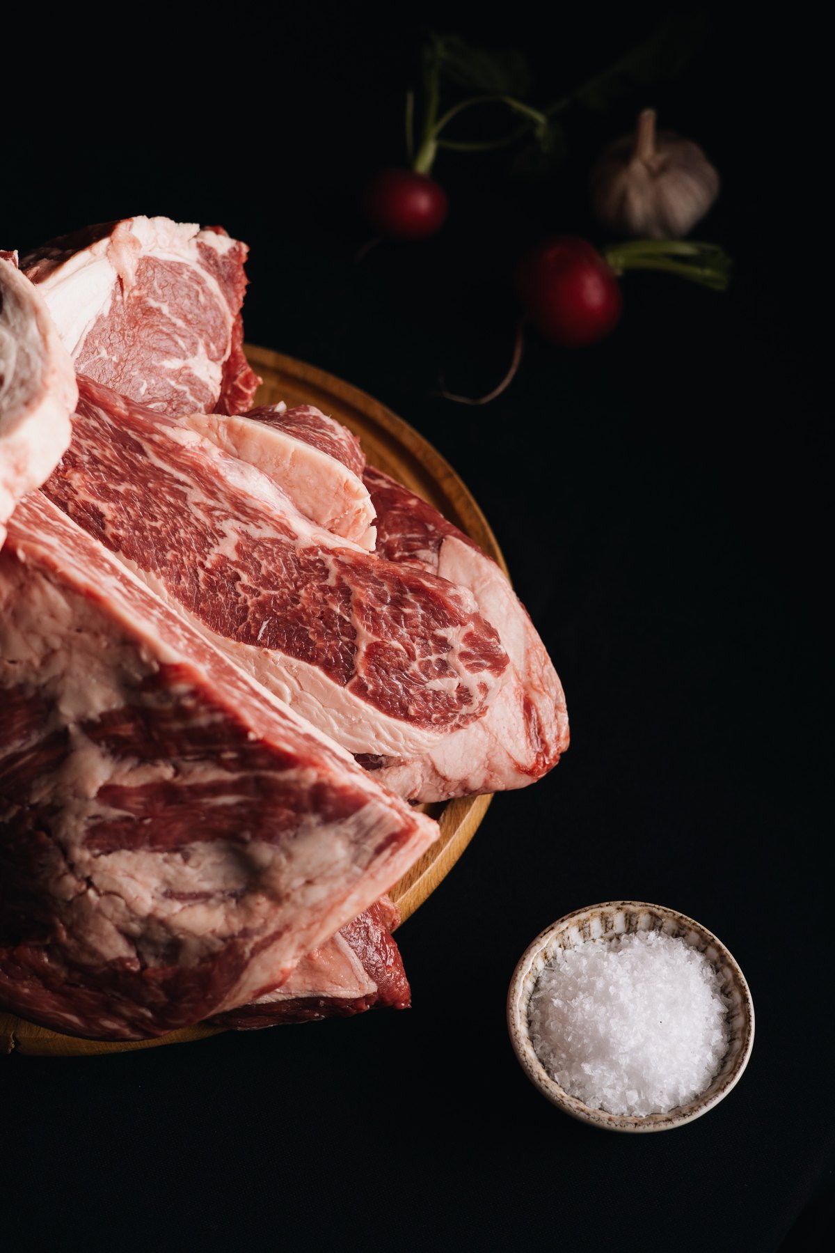 Raw beef cuts on a wooden board beside a bowl of flaky salt