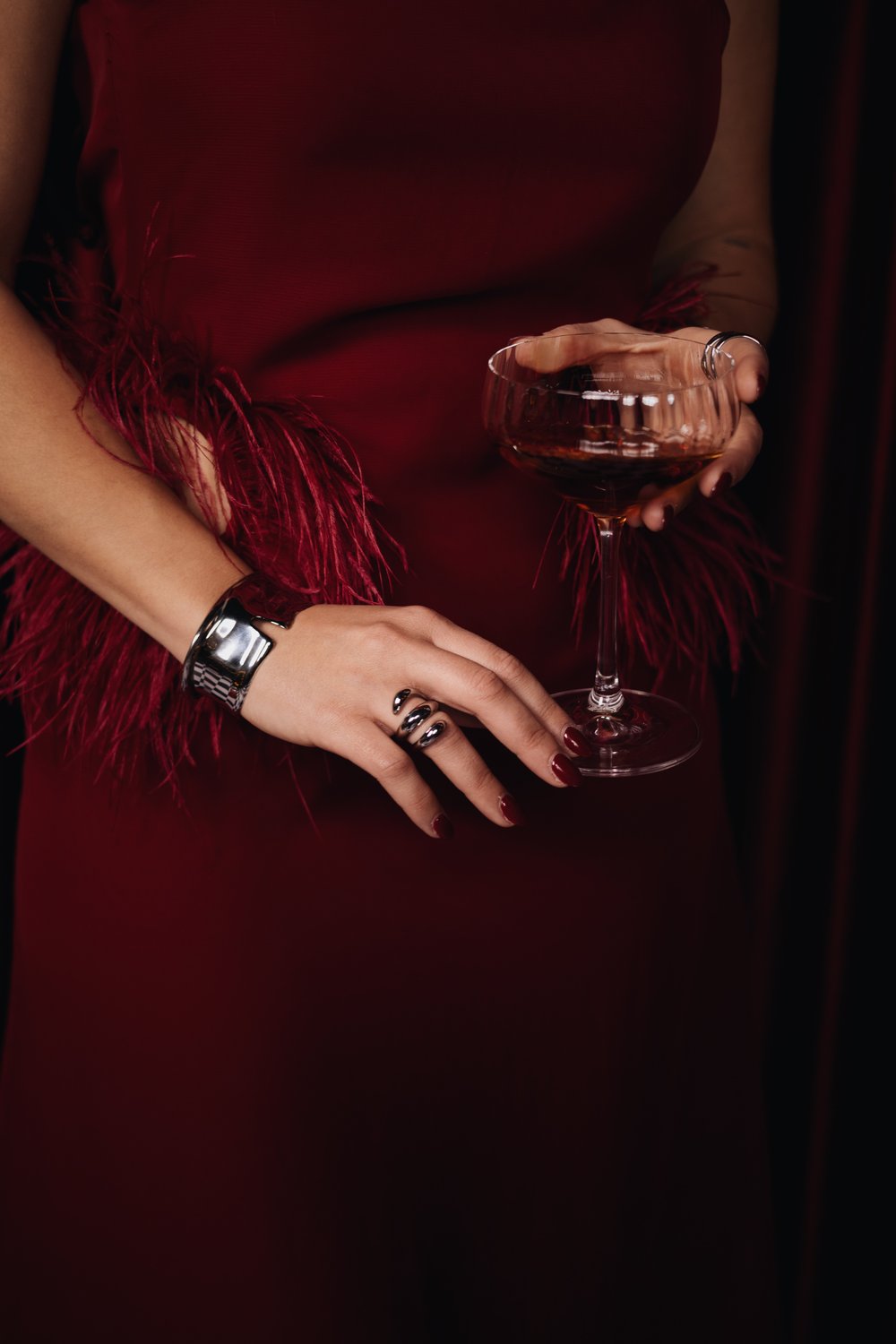 Silver cuff and spiral ring worn with a red feathered dress and a cocktail glass