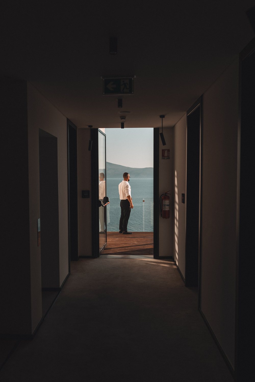 Dark hotel corridor opening onto a guest looking out at the sea