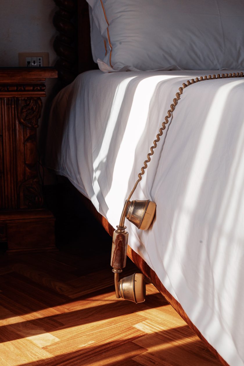 Vintage brass telephone receiver hanging off a sunlit bed