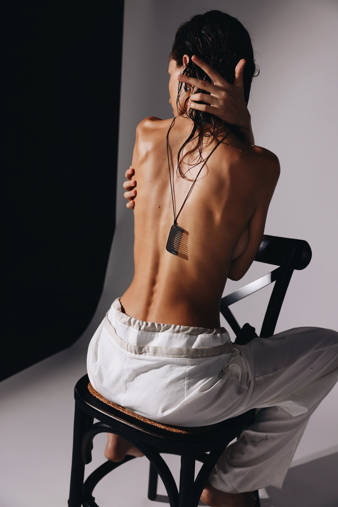 Model seated on a black chair from behind, wearing the Bannu comb pendant with one hand in her wet hair