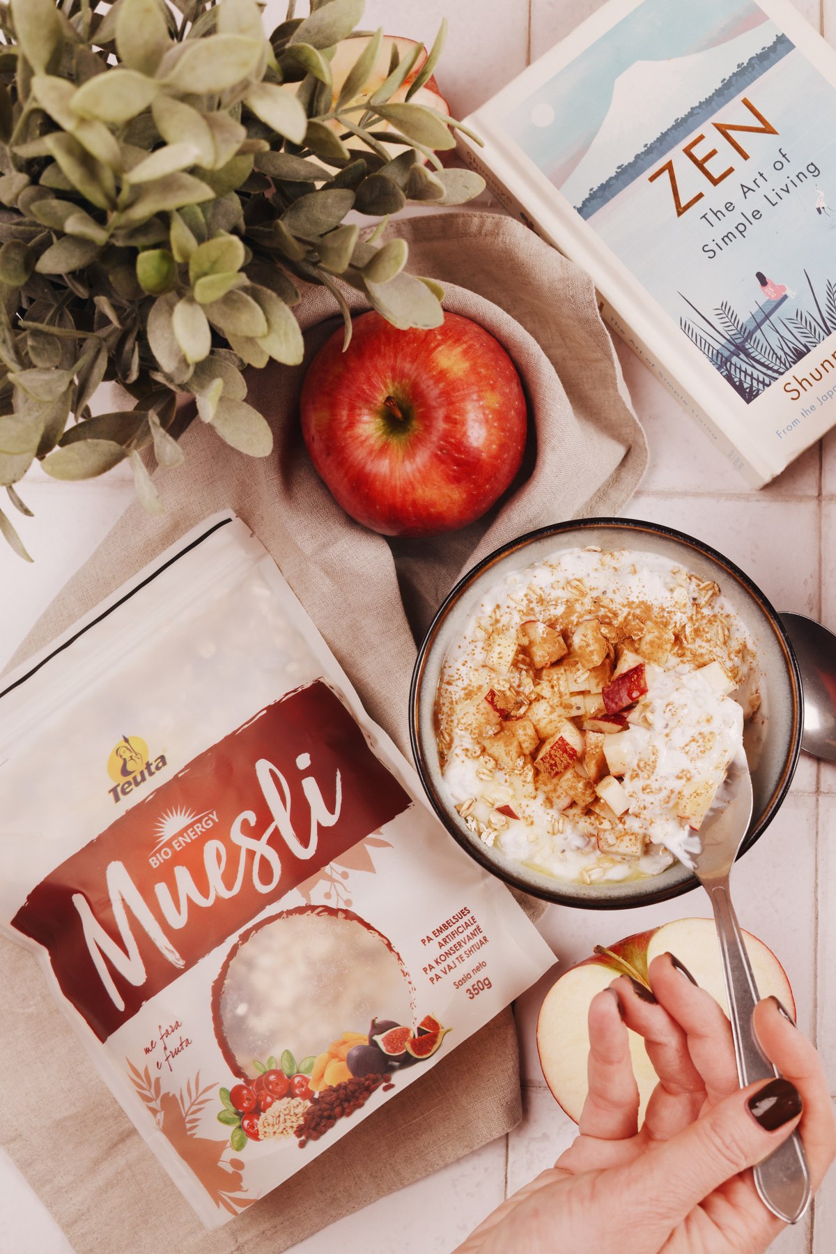 Hand eating overnight muesli with apple and cinnamon beside a Teuta Muesli pack