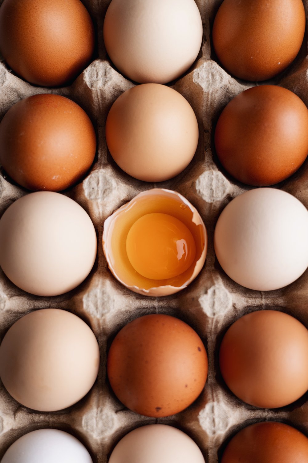 Eggs in a carton with one cracked to show the yolk