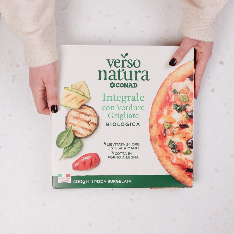 Hands holding a Verso Natura CONAD pizza box on a terrazzo surface